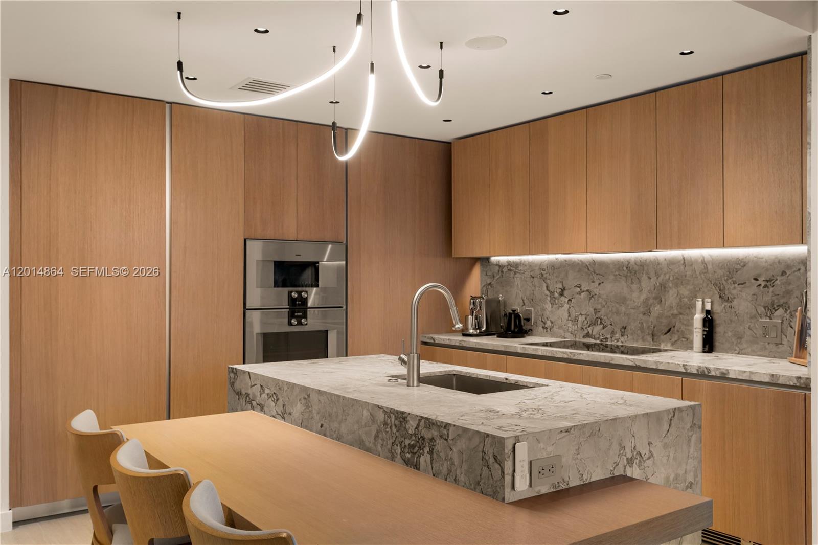 A modern kitchen features wood cabinetry, marble countertops, a central island, and a unique chandelier — 500 Alton Rd # 1601, Miami Beach FL 33139, MIAMI BEACH, FL