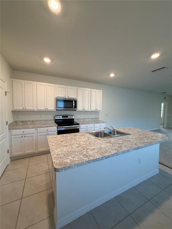 A kitchen features white cabinets, a central island with a sink, and light-colored countertops — 1064 ANDEAN LANE, DAVENPORT, FL