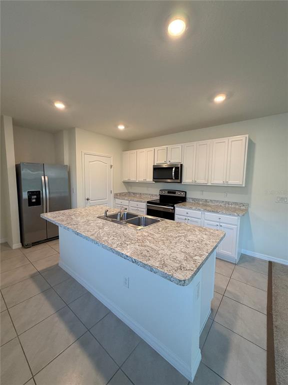 A kitchen features white cabinets, a granite-topped island with a sink, and stainless steel appliances — 1064 ANDEAN LANE, DAVENPORT, FL
