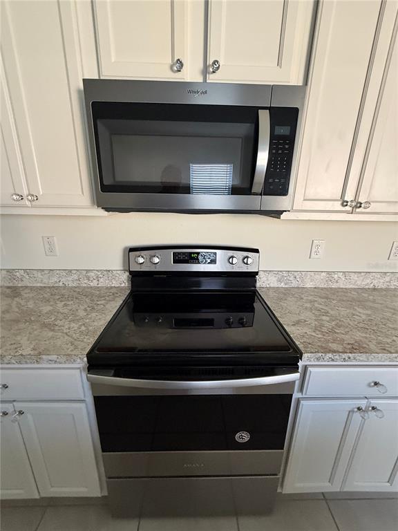 A kitchen features white cabinets, a stainless steel microwave, and a black electric range — 1064 ANDEAN LANE, DAVENPORT, FL