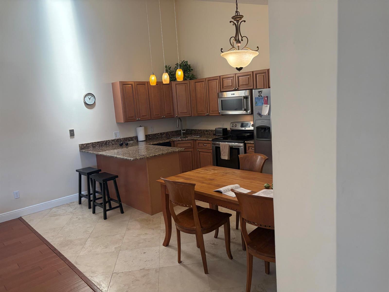 A kitchen with wood cabinets, granite countertops, and a dining table sits on tile flooring — 5654 Golden Eagle Circle, Palm Beach Gardens FL 33418, PALM BEACH GARDENS, FL