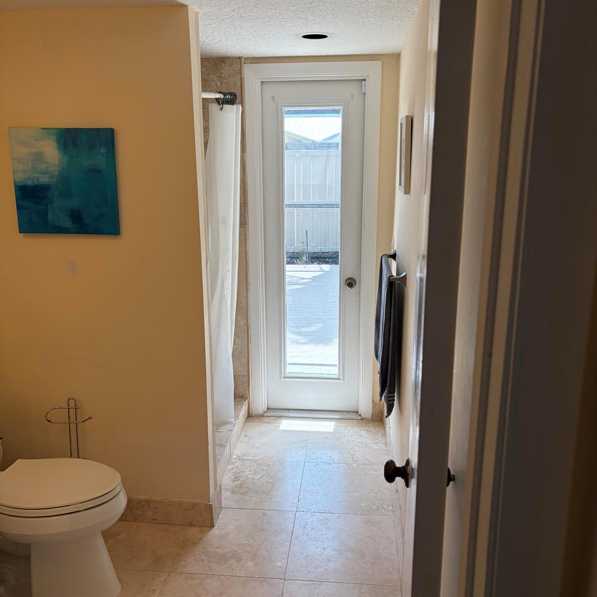 A bathroom with a toilet, shower, tile flooring, and a glass door leading to a patio — 5654 Golden Eagle Circle, Palm Beach Gardens FL 33418, PALM BEACH GARDENS, FL