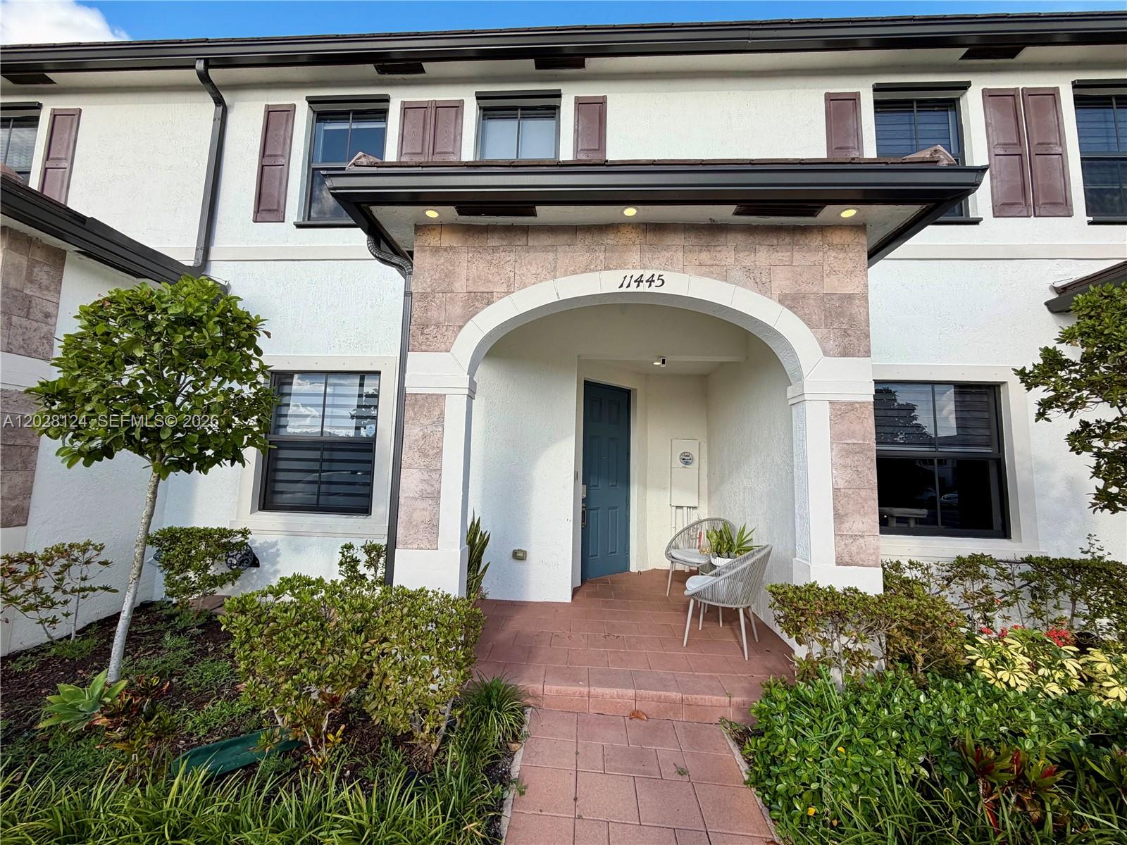 The exterior of a two-story townhouse features a stone-accented arched entryway and a blue door — 11445 W 33rd Ln, Hialeah FL 33018, HIALEAH, FL