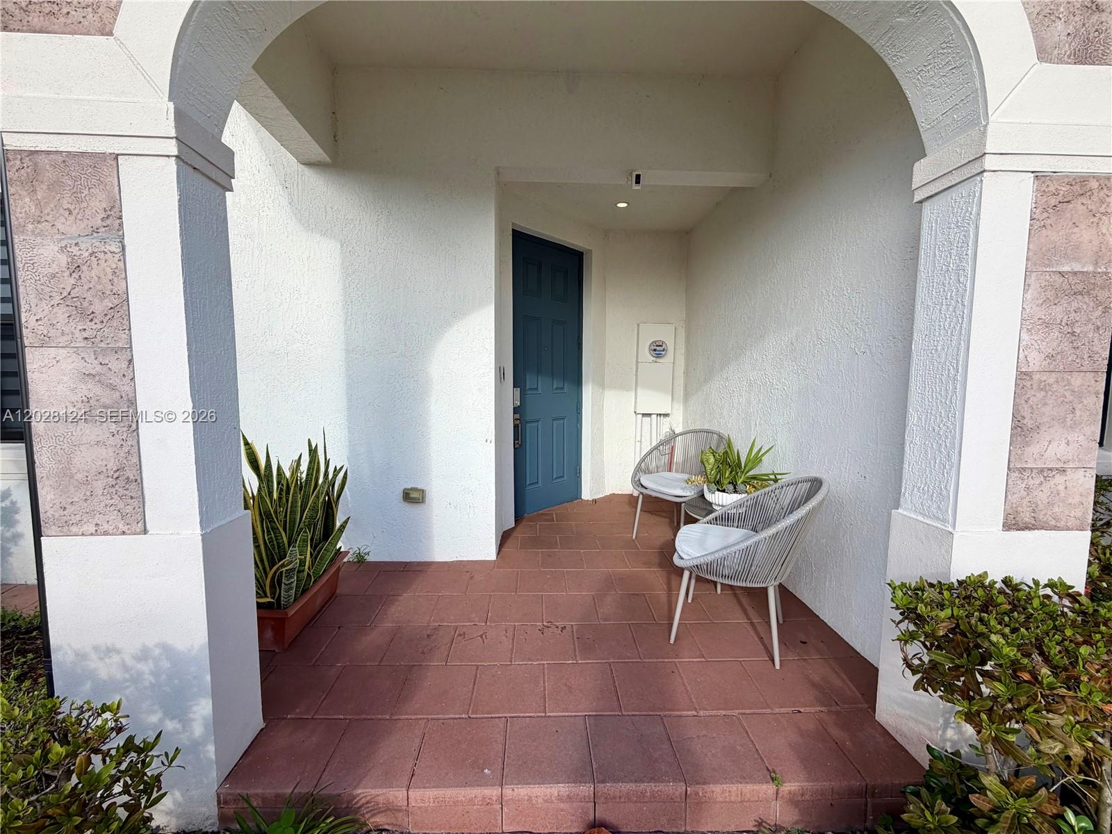 A covered entryway features a blue door, tiled flooring, and two gray patio chairs — 11445 W 33rd Ln, Hialeah FL 33018, HIALEAH, FL