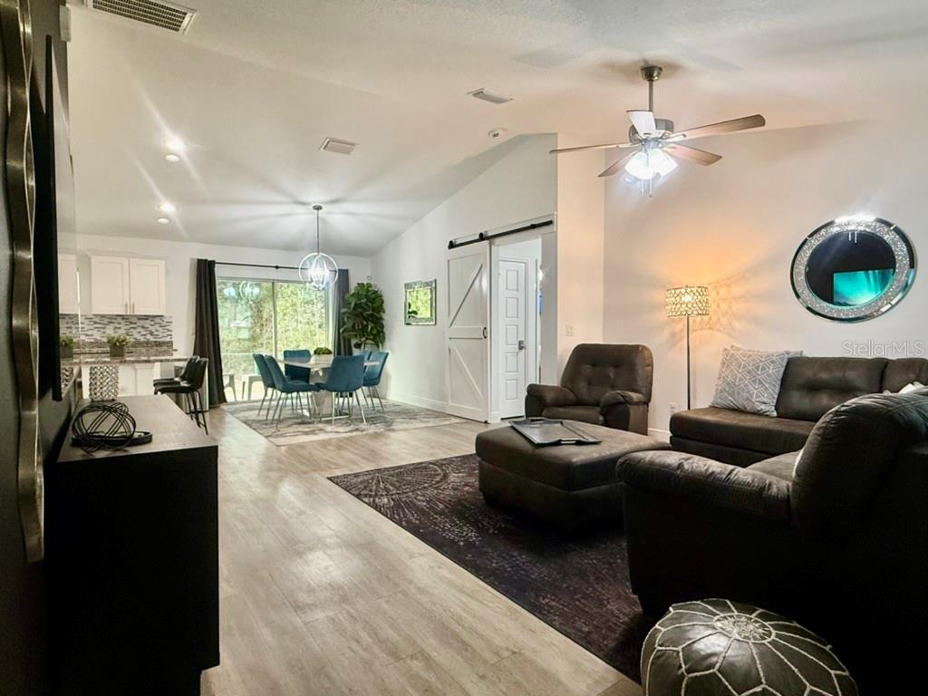 A living room and dining area feature wood-look flooring, a sliding barn door, and furniture — 5653 PECAN ROAD, OCALA, FL