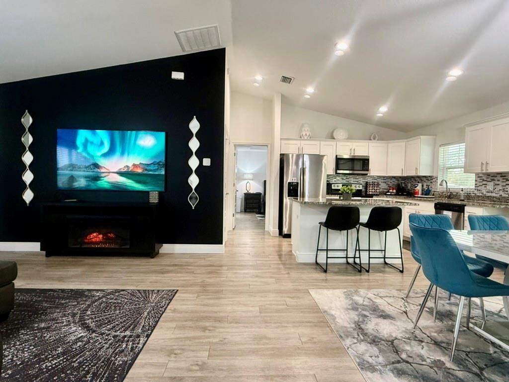 An open-concept living room and kitchen featuring a black accent wall with a fireplace — 5653 PECAN ROAD, OCALA, FL