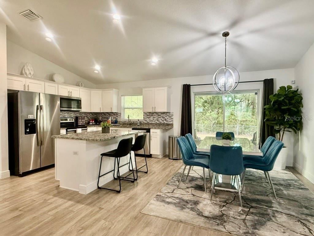 A kitchen with white cabinets and a granite island opens to a dining area — 5653 PECAN ROAD, OCALA, FL