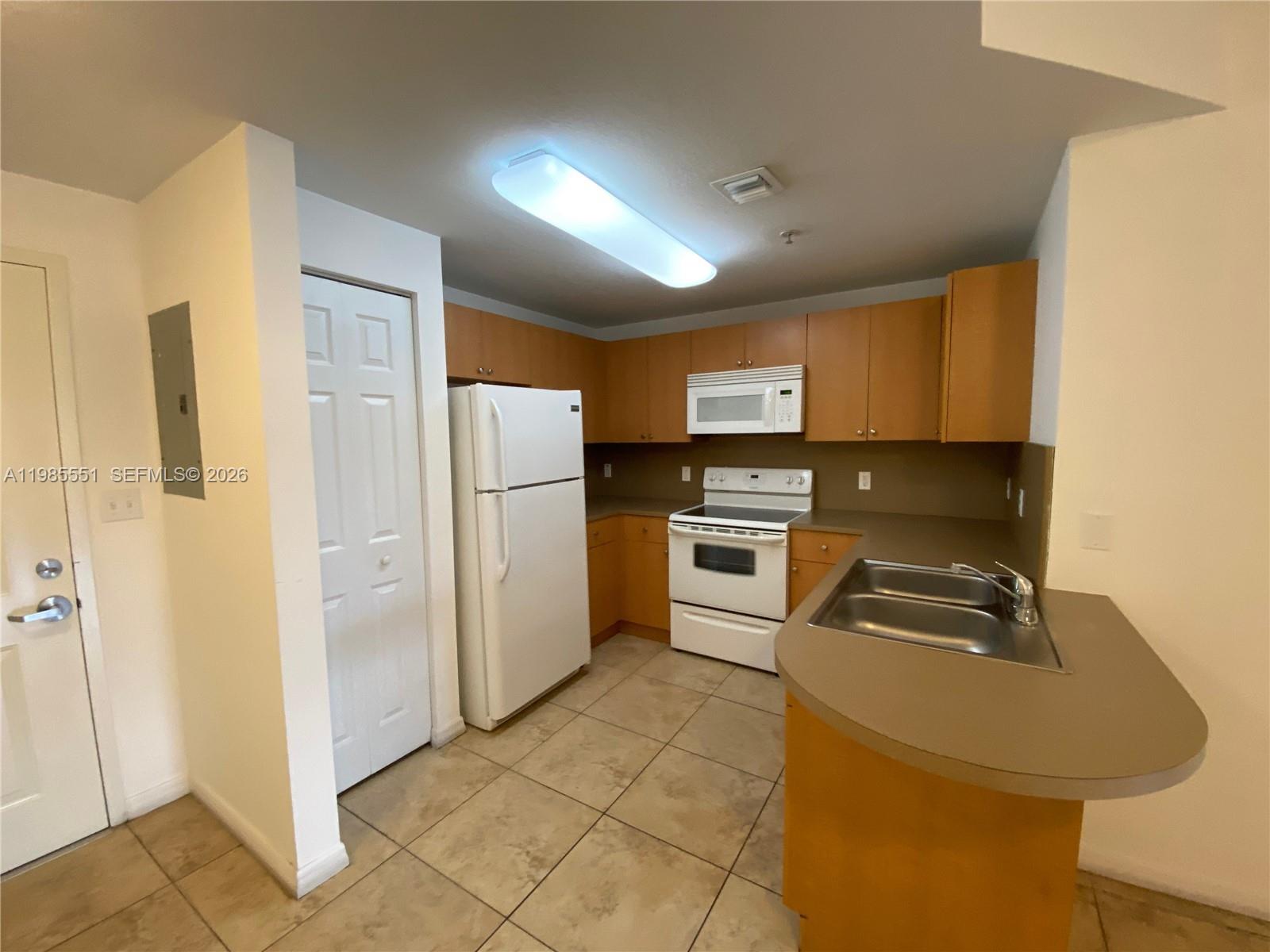 A kitchen features light wood cabinets, white appliances, tan countertops, and beige tile flooring — 435 SW 12th Ave # 605, Miami FL 33130, MIAMI, FL