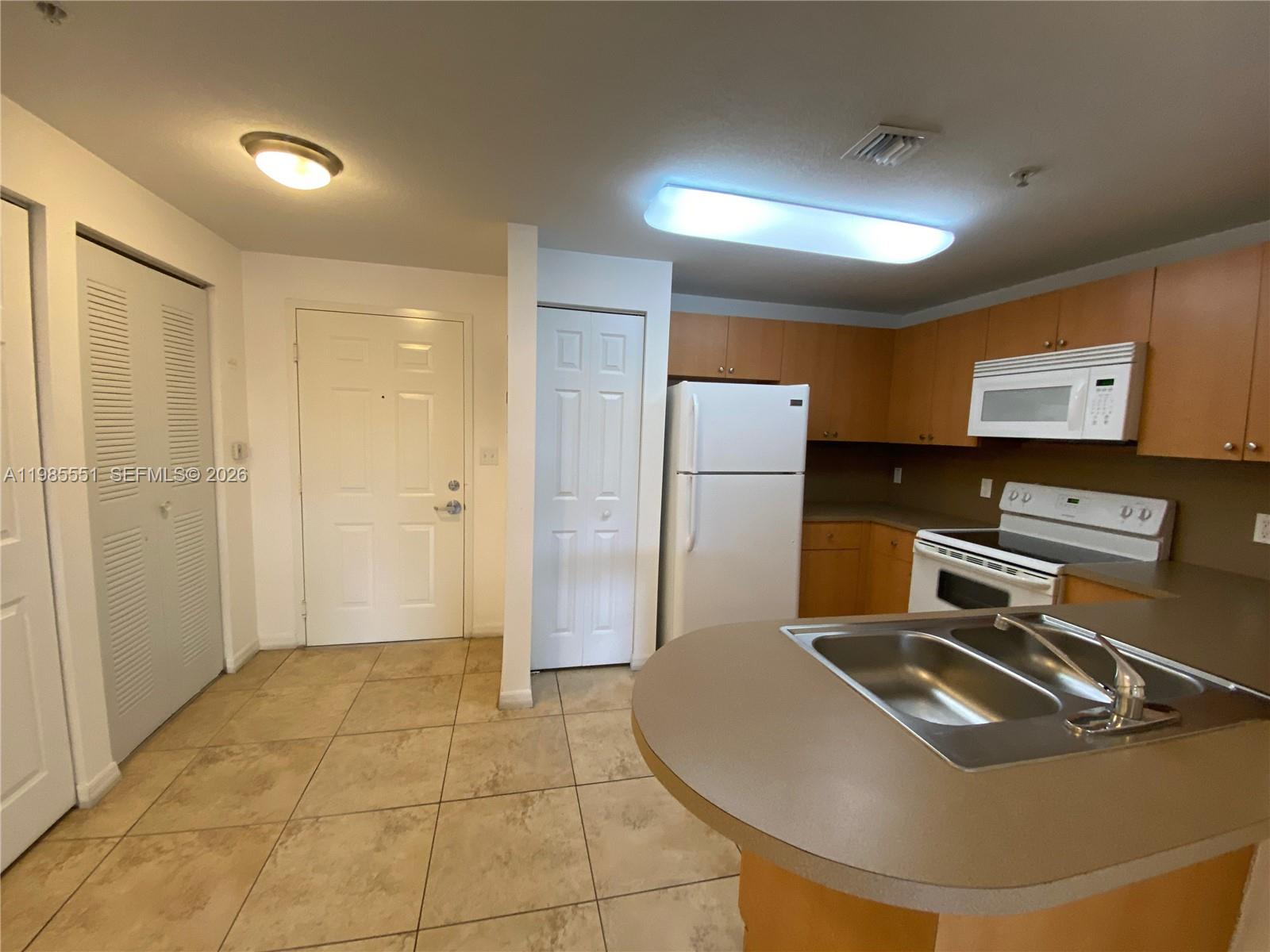 A kitchen features light wood cabinets, white appliances, a double sink, and beige tile flooring — 435 SW 12th Ave # 605, Miami FL 33130, MIAMI, FL
