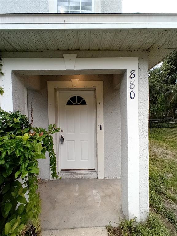 A white front door with a small arched window is set under a covered porch — 880 E COLUMBIA AVENUE, KISSIMMEE, FL