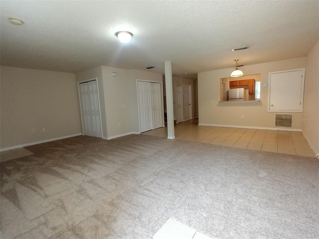 An interior view shows a living room with carpeted flooring and a tiled kitchen area — 880 E COLUMBIA AVENUE, KISSIMMEE, FL