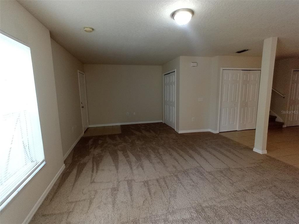 A carpeted living room features a window, two sets of closet doors, and a support column — 880 E COLUMBIA AVENUE, KISSIMMEE, FL