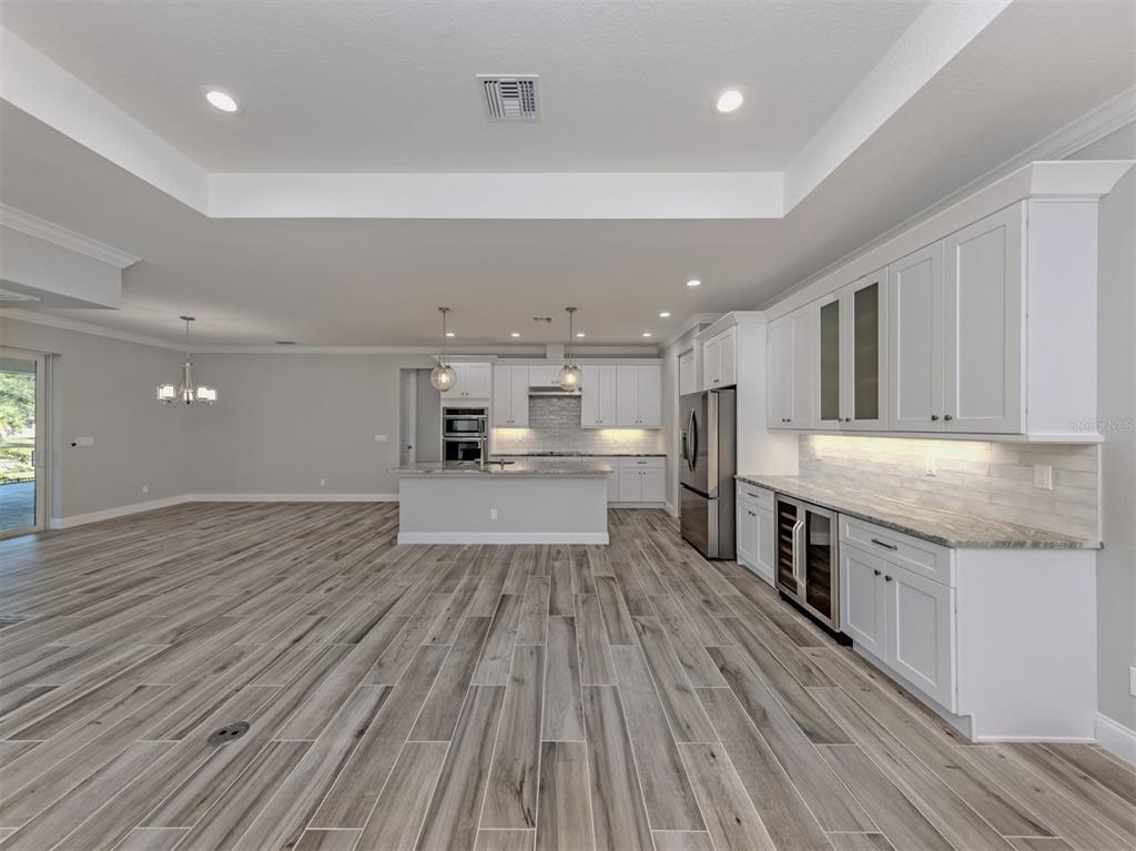 A modern kitchen features white cabinetry, stainless steel appliances, and wood-look tile flooring — 3423 KNOX TERRACE, PORT CHARLOTTE, FL