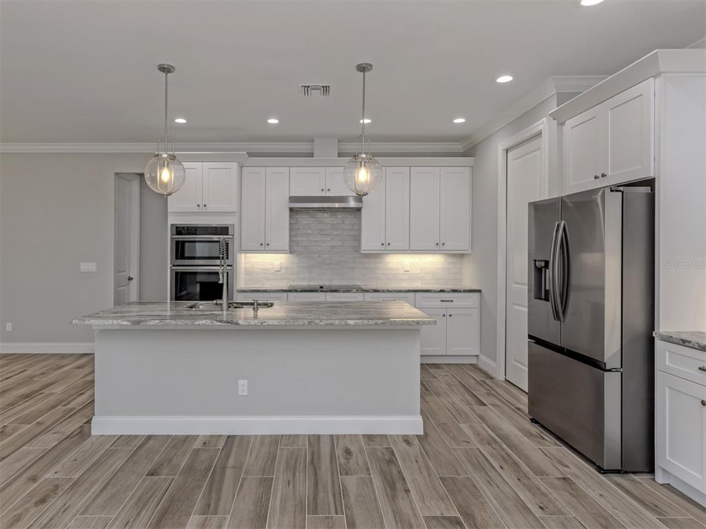 A modern kitchen features white cabinets, stainless steel appliances, a stone island, and wood-look flooring — 3423 KNOX TERRACE, PORT CHARLOTTE, FL