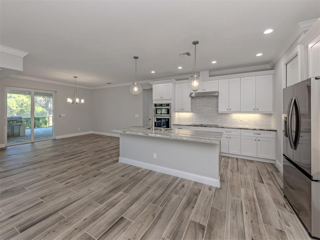 A modern kitchen features white cabinetry, a stone island, and wood-look tile flooring — 3423 KNOX TERRACE, PORT CHARLOTTE, FL