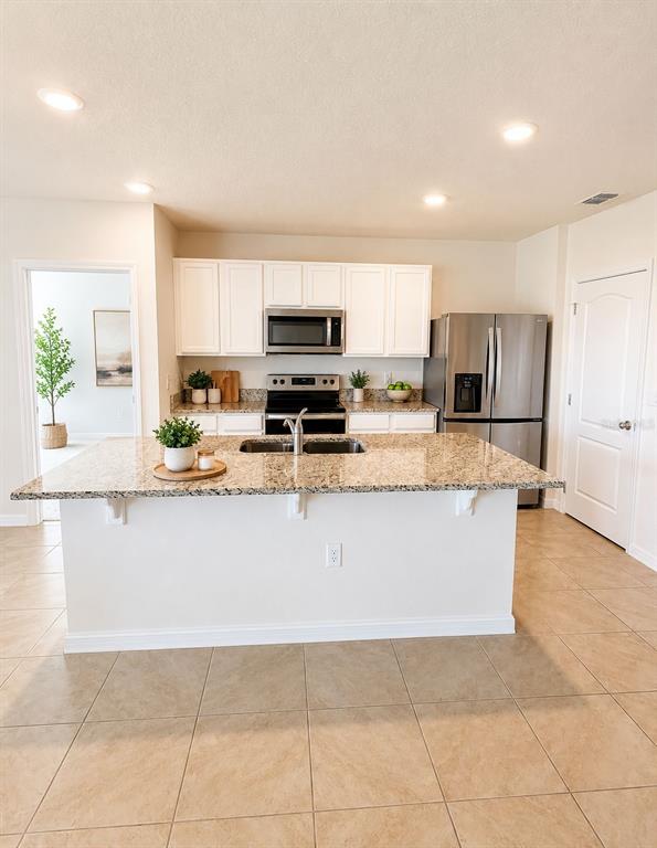 A kitchen features white cabinets, stainless steel appliances, a granite island, and tile flooring — 1071 BROOKLET DRIVE, DAVENPORT, FL