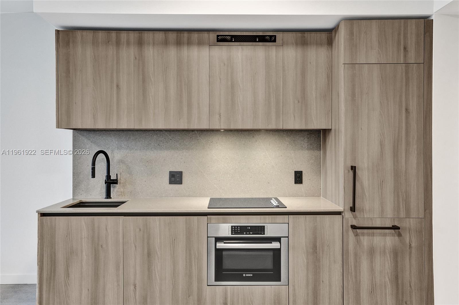 A modern kitchen features wood-grain cabinetry, a stone backsplash, a sink, and a built-in oven — 121 NE 5th Street # 807, Miami FL 33132, MIAMI, FL