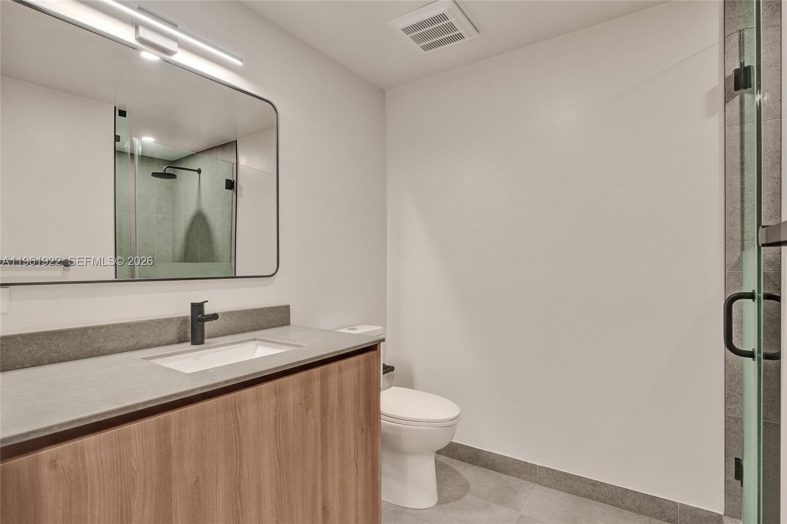 A modern bathroom features a wood vanity, gray stone countertop, and a glass-enclosed shower — 121 NE 5th Street # 807, Miami FL 33132, MIAMI, FL