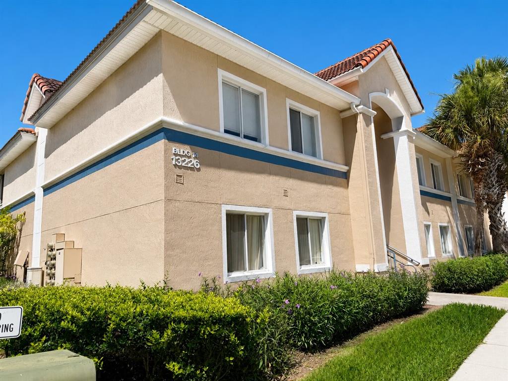 A two-story apartment building exterior features tan stucco walls, a tiled roof, and parking spaces — 13226 GALICIA STREET UNIT 102, ORLANDO, FL
