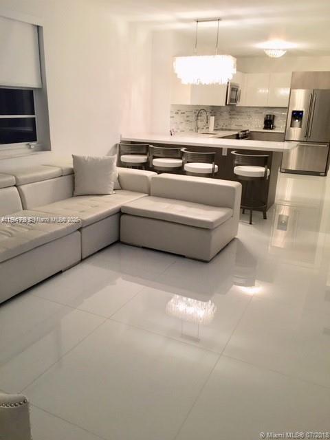 A modern open-concept living room features a white sectional sofa, glossy tile floors, and kitchen — 100 LINCOLN RD # 711, Miami Beach FL 33139, MIAMI BEACH, FL