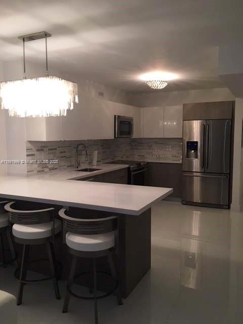 A modern kitchen features white cabinetry, stainless steel appliances, a breakfast bar, and pendant lighting — 100 LINCOLN RD # 711, Miami Beach FL 33139, MIAMI BEACH, FL