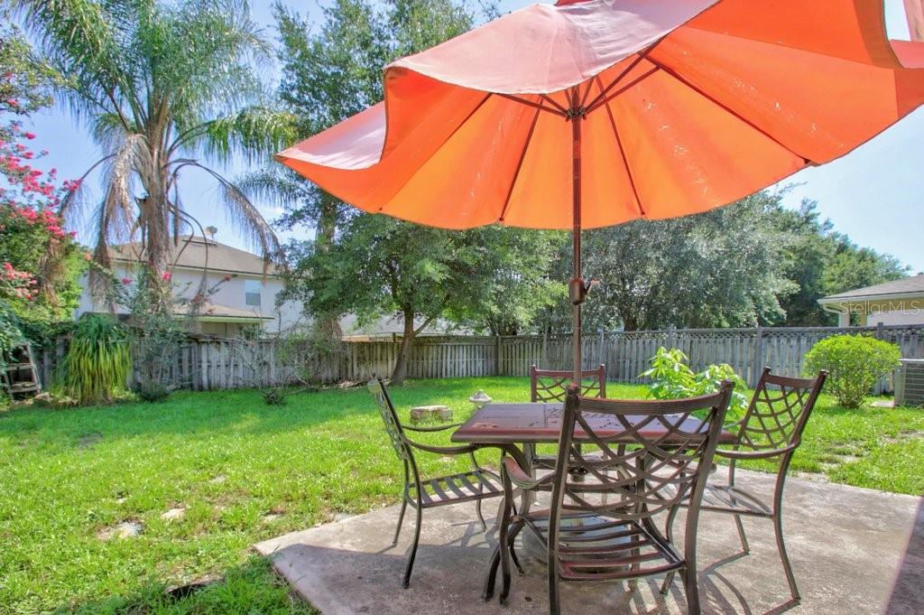A patio with a metal dining set and orange umbrella sits in a grassy backyard — 828 CRYSTAL SPRING WAY, ST AUGUSTINE, FL