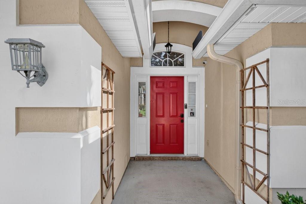 A covered entryway features a bright red front door with side windows and wall-mounted trellises — 828 CRYSTAL SPRING WAY, ST AUGUSTINE, FL