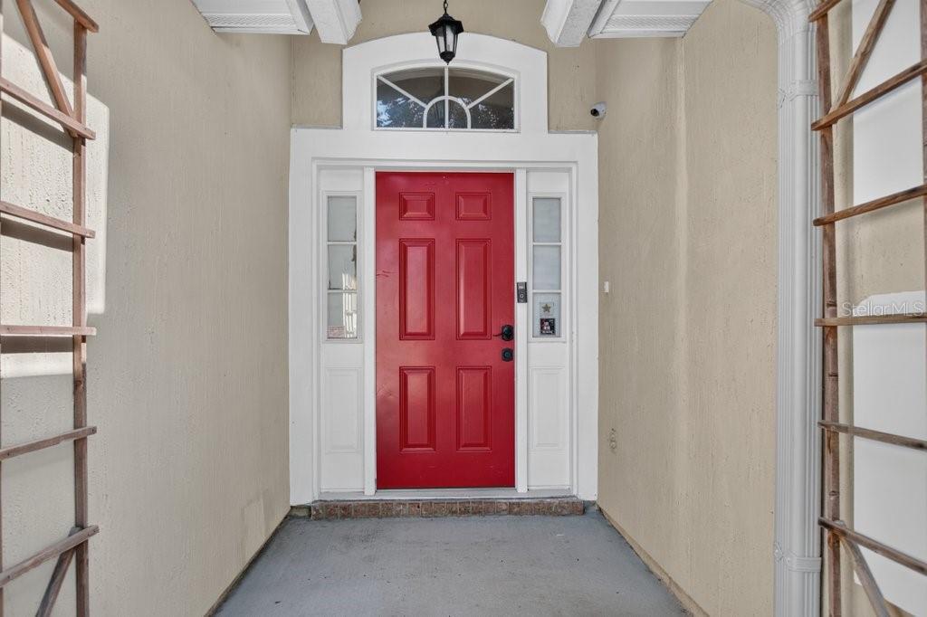A red front door with a transom window is framed by white trim and trellises — 828 CRYSTAL SPRING WAY, ST AUGUSTINE, FL