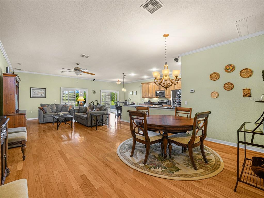 An open-concept living and dining area features hardwood floors, light green walls, and wooden furniture — 4052 PHOENICIAN WAY, WINTER HAVEN, FL