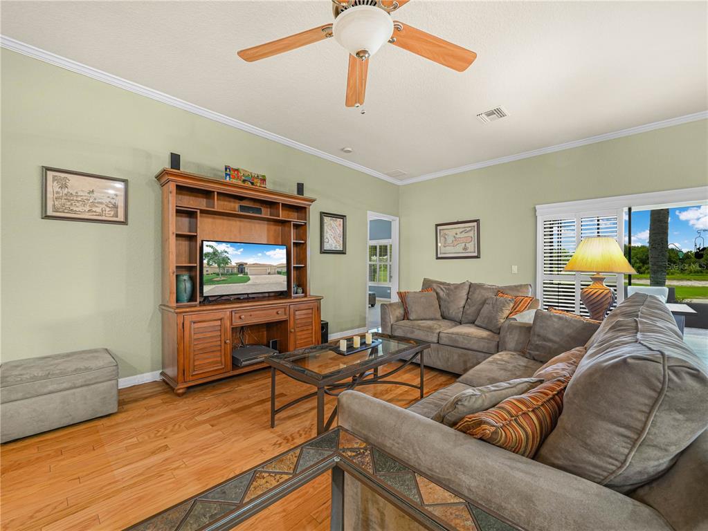 A living room with light green walls, wood flooring, a ceiling fan, and brown furniture — 4052 PHOENICIAN WAY, WINTER HAVEN, FL