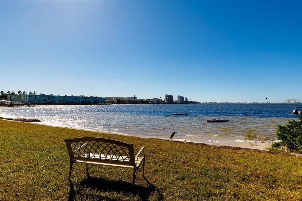 A metal bench sits on a grassy lawn overlooking a bay with distant buildings — 2700 BAYSHORE BOULEVARD UNIT 588, DUNEDIN, FL