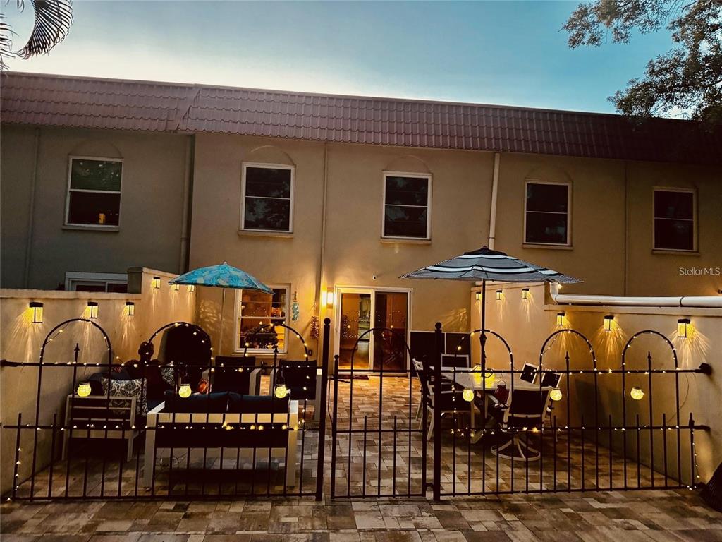 A paved patio features outdoor furniture, umbrellas, and decorative string lights enclosed by a metal fence — 2700 BAYSHORE BOULEVARD UNIT 588, DUNEDIN, FL