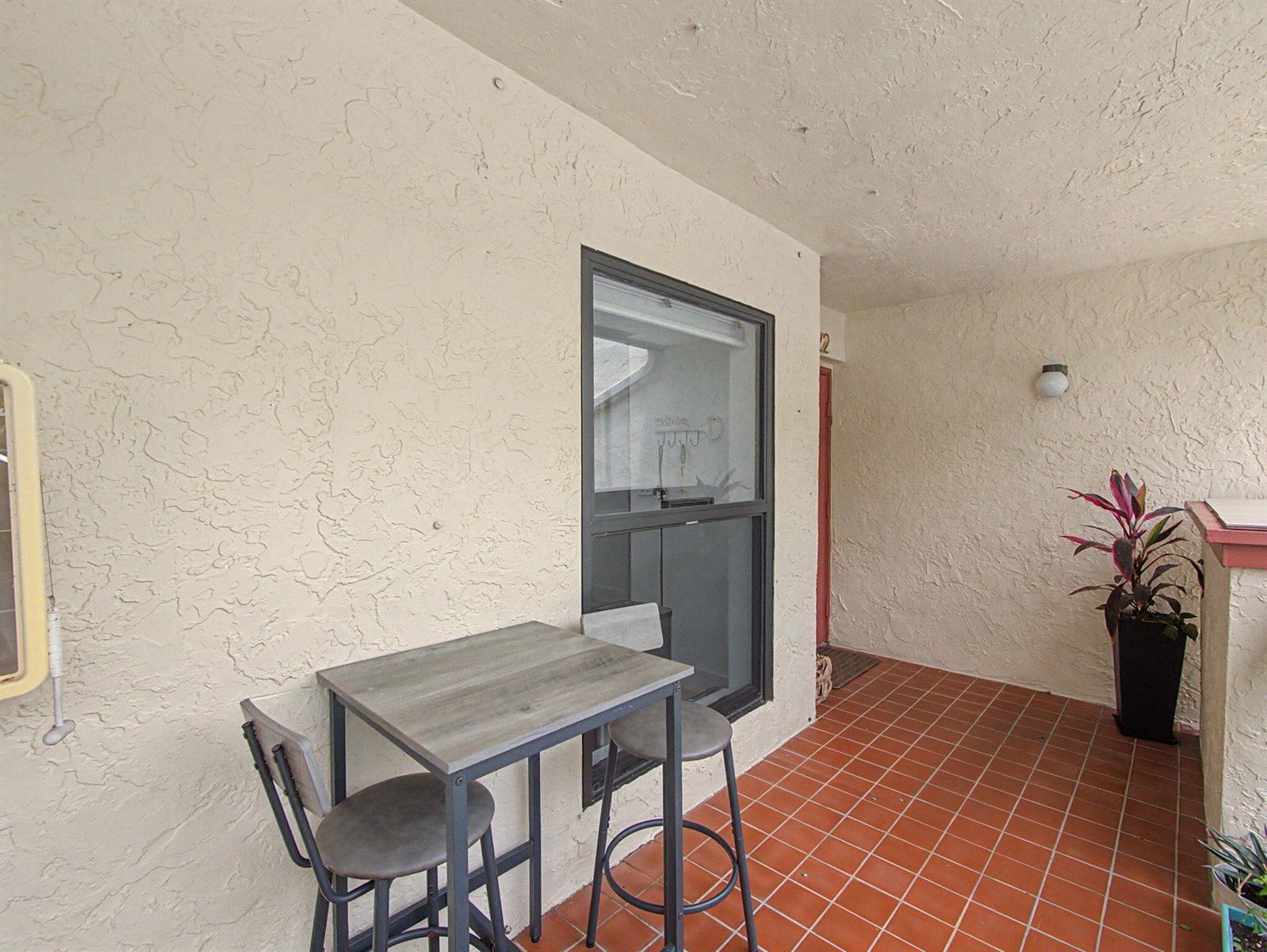 A small patio features a bistro set, tiled flooring, and textured beige walls — 5154 Oak Hill Lane # 1022, Delray Beach FL 33484, DELRAY BEACH, FL