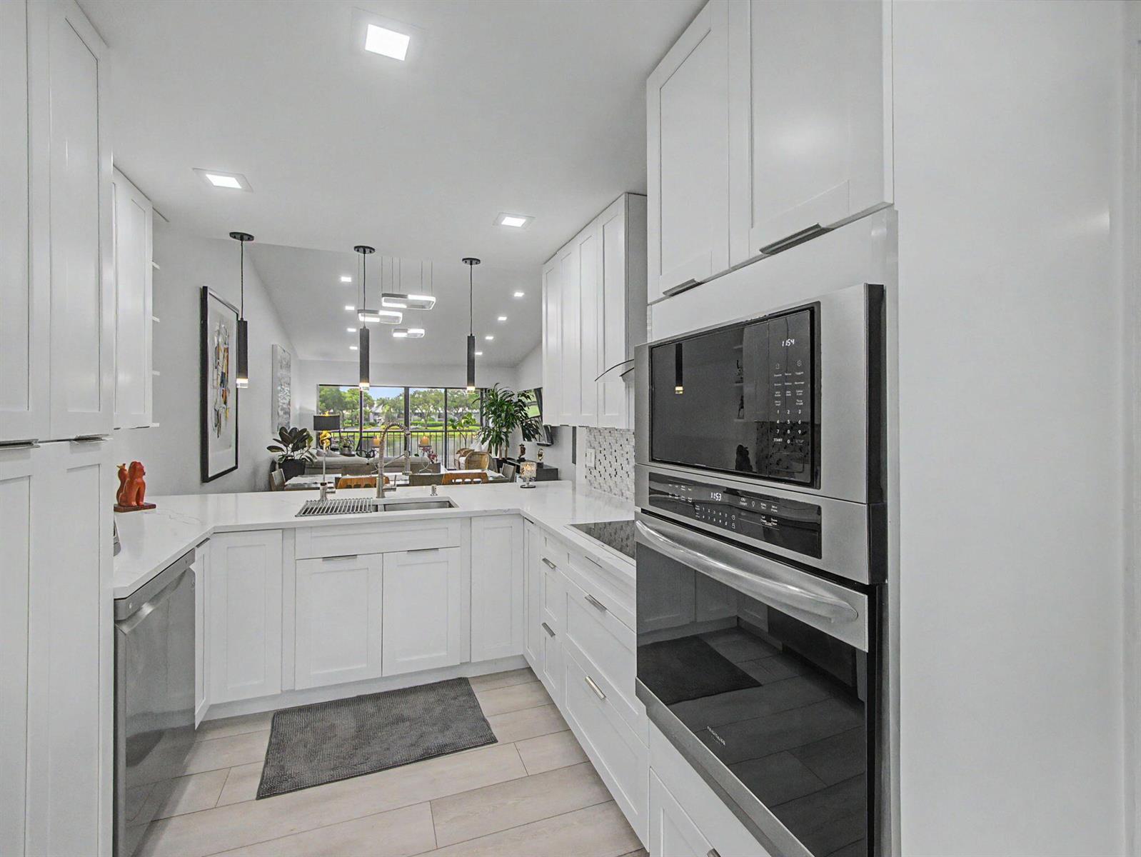 A modern white kitchen features stainless steel appliances, quartz countertops, and an open-concept layout — 5154 Oak Hill Lane # 1022, Delray Beach FL 33484, DELRAY BEACH, FL