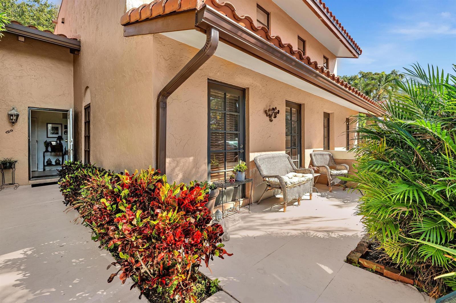 A stucco house exterior features a covered patio with wicker chairs and colorful croton plants — 9050 Jacaranda Lane # 3, Plantation FL 33324, PLANTATION, FL