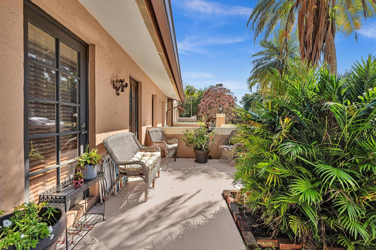 A sunlit outdoor patio features wicker furniture, potted plants, and a view of palm trees — 9050 Jacaranda Lane # 3, Plantation FL 33324, PLANTATION, FL