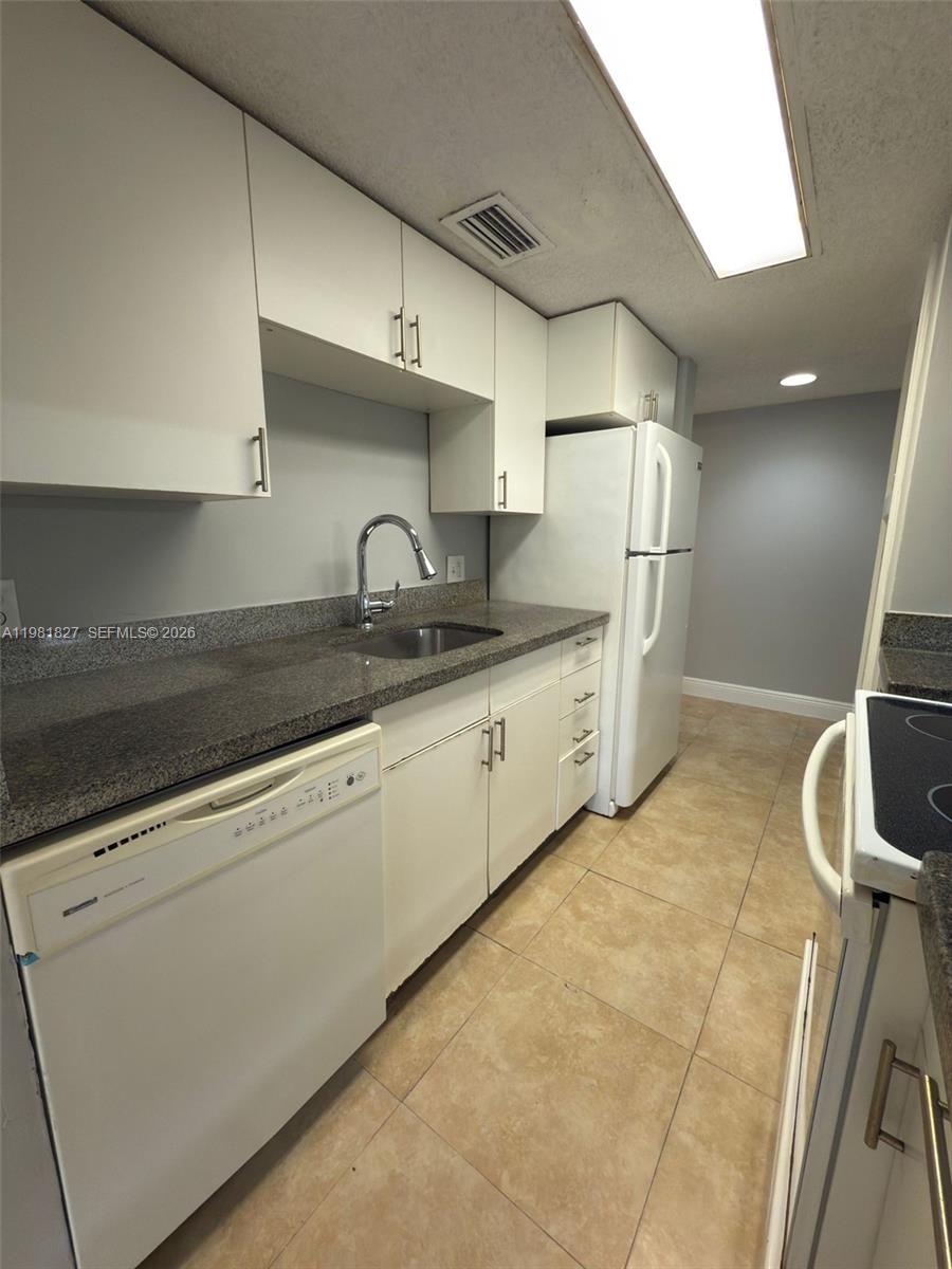 This galley kitchen features white cabinets, granite countertops, a stainless steel sink, and tile flooring — 4521 W Mcnab Rd # 11, Pompano Beach FL 33069, POMPANO BEACH, FL