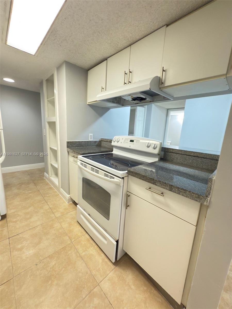 A galley kitchen features white cabinets, granite countertops, a white range, and tile flooring — 4521 W Mcnab Rd # 11, Pompano Beach FL 33069, POMPANO BEACH, FL