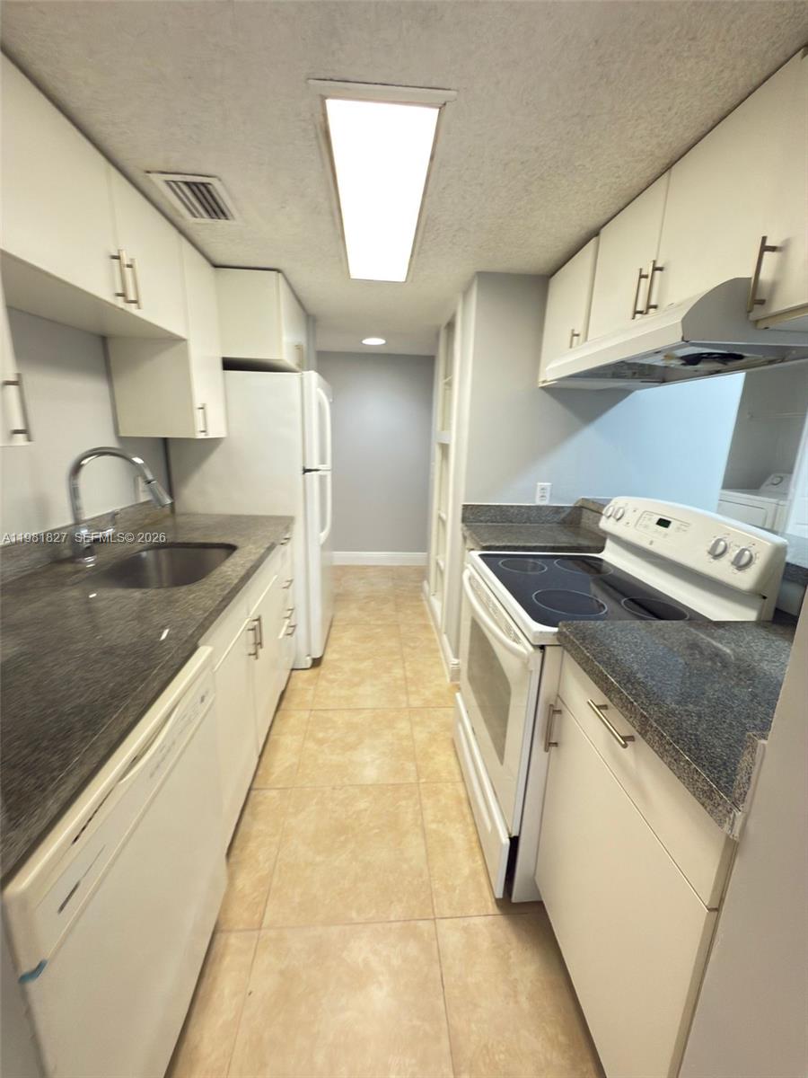 A galley kitchen features white cabinets, granite countertops, and white appliances — 4521 W Mcnab Rd # 11, Pompano Beach FL 33069, POMPANO BEACH, FL