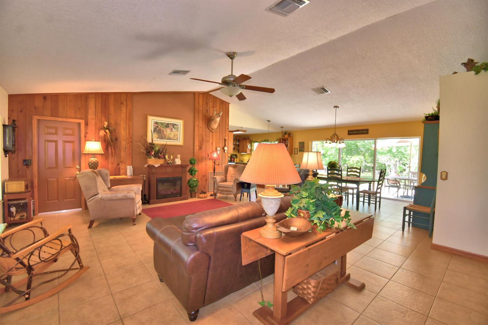 A living room with wood-paneled walls, a fireplace, tile floors, and a dining area beyond — 32801 Hwy 441 N # 36, Okeechobee FL 34972, OKEECHOBEE, FL