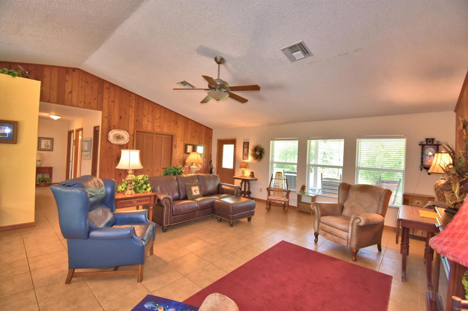 A living room features wood-paneled walls, tile flooring, a ceiling fan, and leather furniture — 32801 Hwy 441 N # 36, Okeechobee FL 34972, OKEECHOBEE, FL