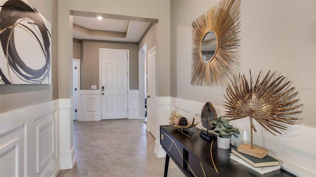 An entryway features white wainscoting, tile flooring, a black console table, and gold wall decor — 32645 DULUTH DRIVE, WESLEY CHAPEL, FL