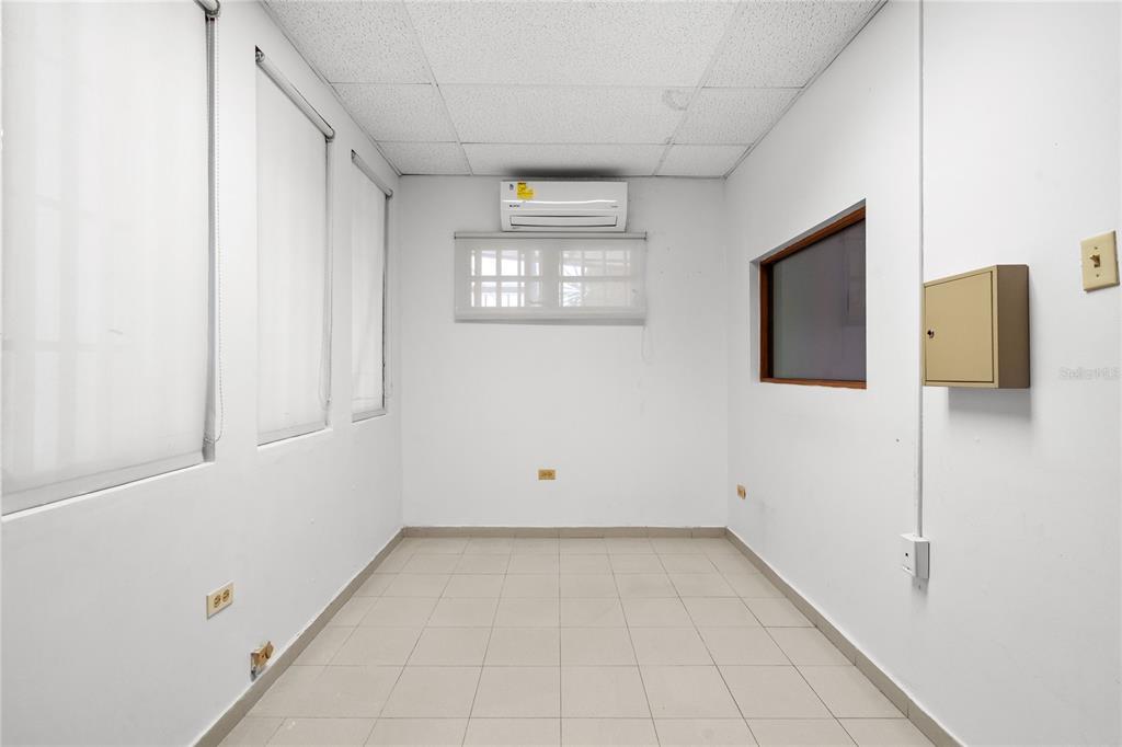 An empty office room features white walls, tiled flooring, a window, and a wall-mounted air conditioner — 141 O'NEILL, SAN JUAN, PR
