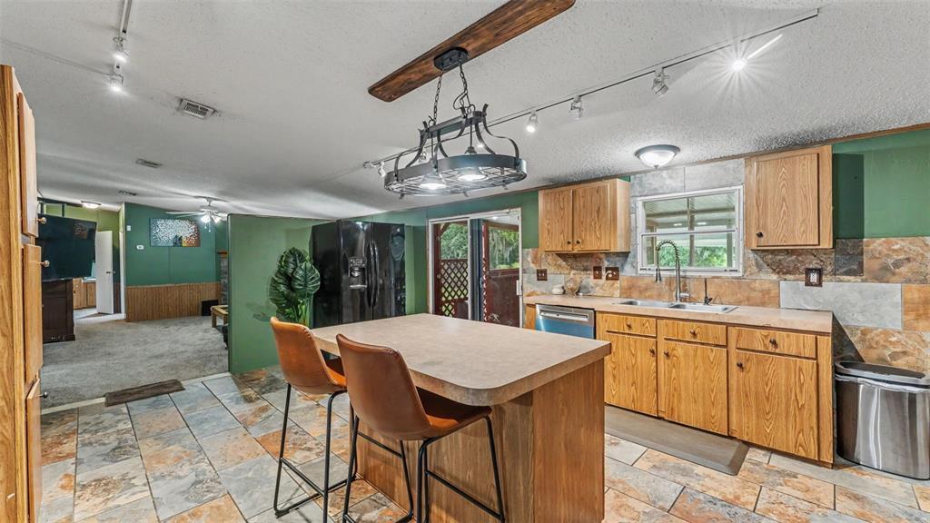 A kitchen features wood cabinets, a central island with two chairs, and slate tile flooring — 6702 FORESTVIEW LANE, LAKELAND, FL