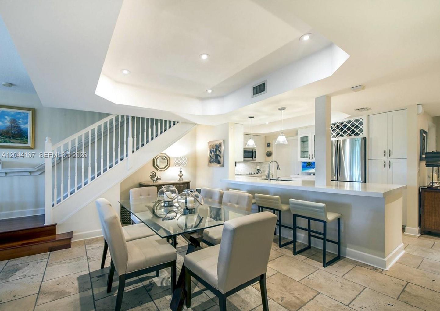 A dining area with a glass table and chairs sits beside a kitchen breakfast bar — 7622 SW 102nd St # 120, Pinecrest FL 33156, PINECREST, FL