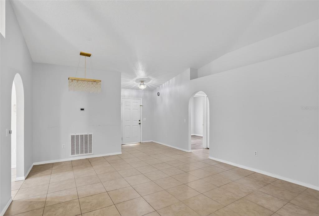 An open-concept dining area features light tile flooring, white walls, and a crystal chandelier — 432 BARLYN AVENUE, HAINES CITY, FL