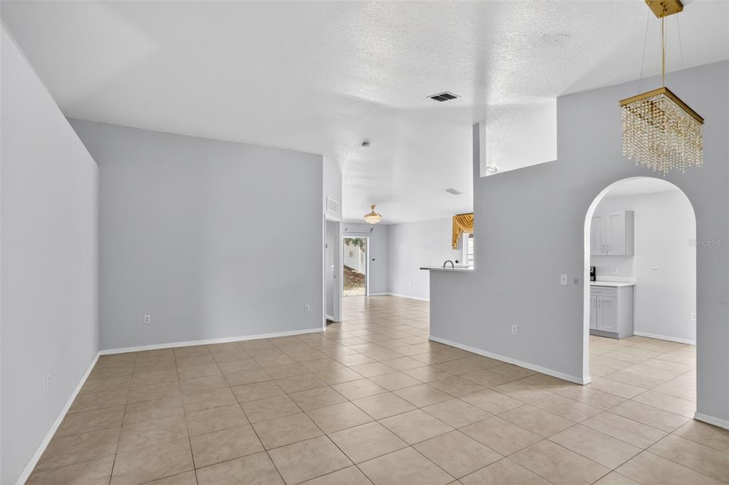 A spacious living area with light-colored tile flooring, gray walls, and an arched kitchen entryway — 432 BARLYN AVENUE, HAINES CITY, FL