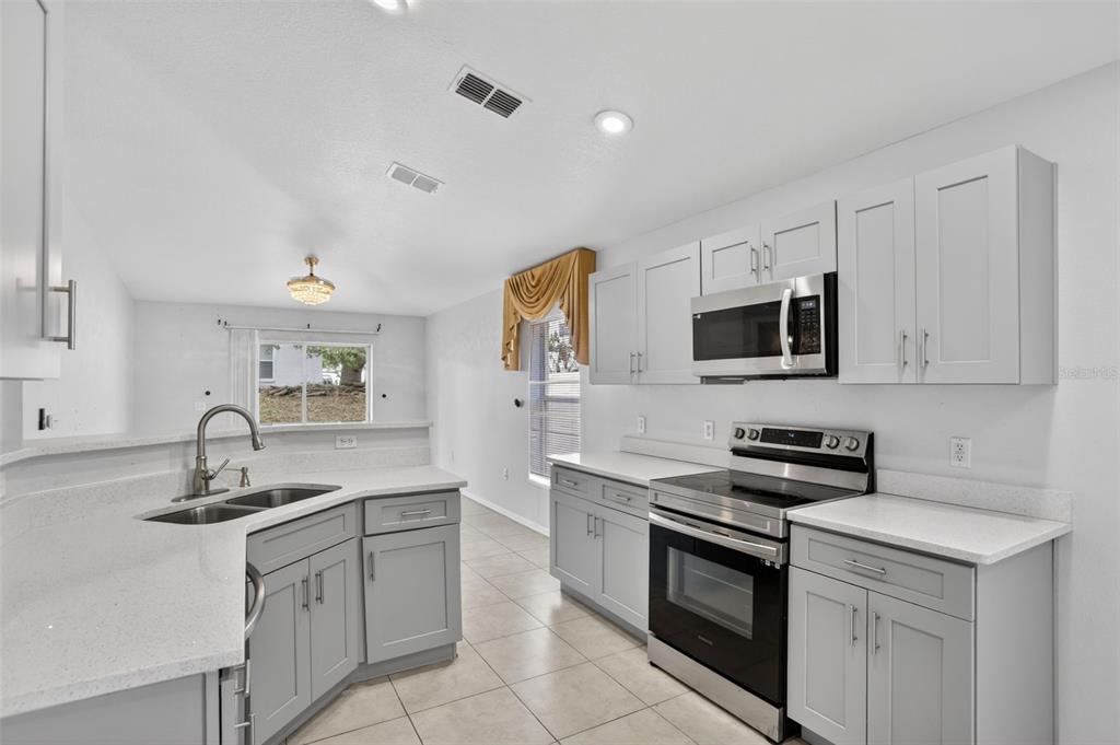A kitchen with gray cabinets, white countertops, stainless steel appliances, and light-colored tile flooring — 432 BARLYN AVENUE, HAINES CITY, FL