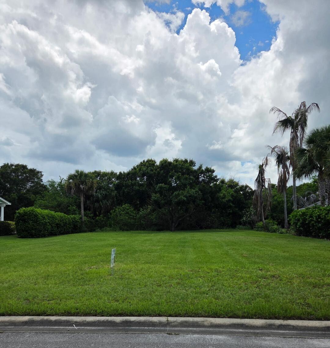 A vacant, grassy residential lot is bordered by trees and shrubs under a cloudy sky — 6385 Tropical Way, Vero Beach FL 32967, VERO BEACH, FL