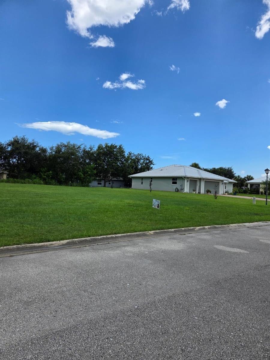 A vacant grassy lot sits next to a single-story house under a blue sky — 6385 Tropical Way, Vero Beach FL 32967, VERO BEACH, FL